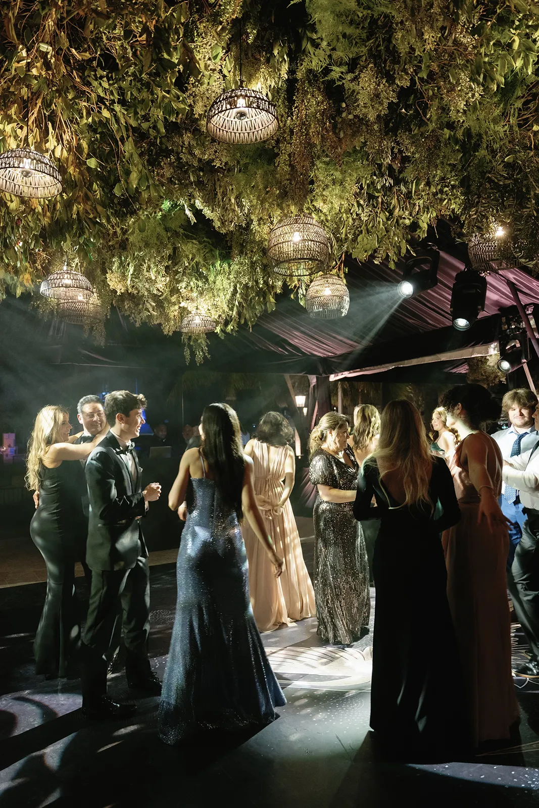 Wedding guests dancing beneath a lush greenery ceiling with hanging lights at a luxury Fisher Island reception