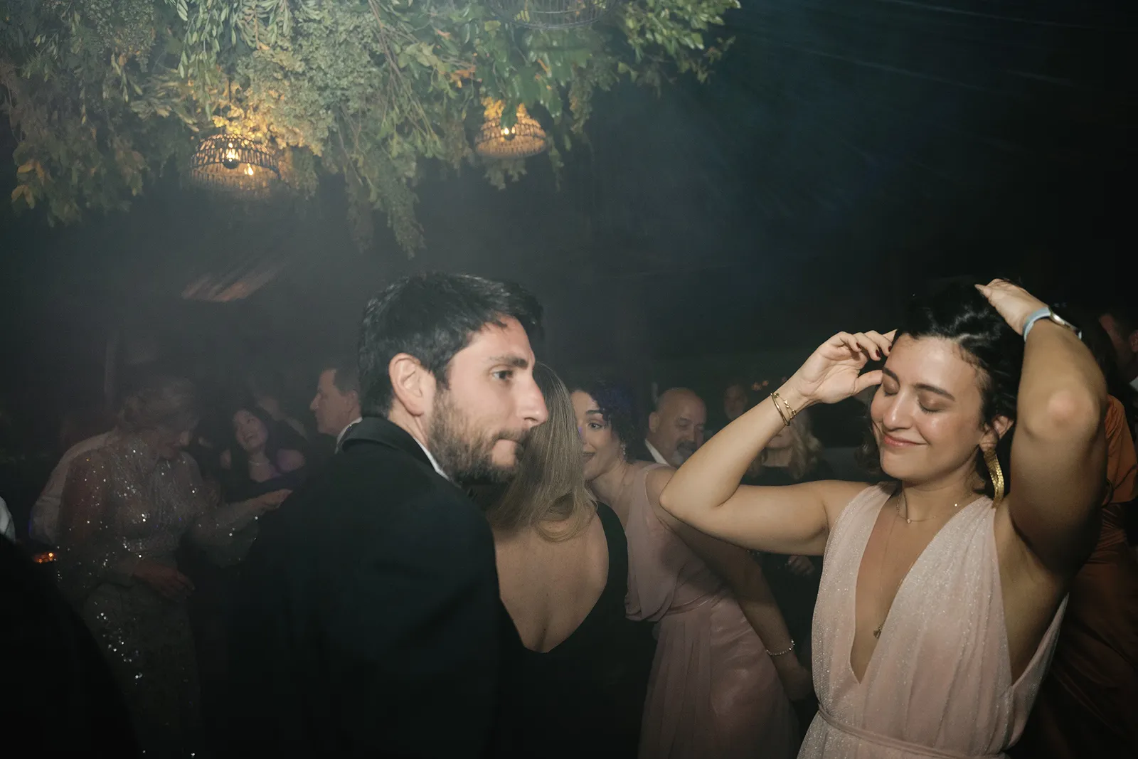 Wedding guests dancing beneath hanging greenery and warm lights