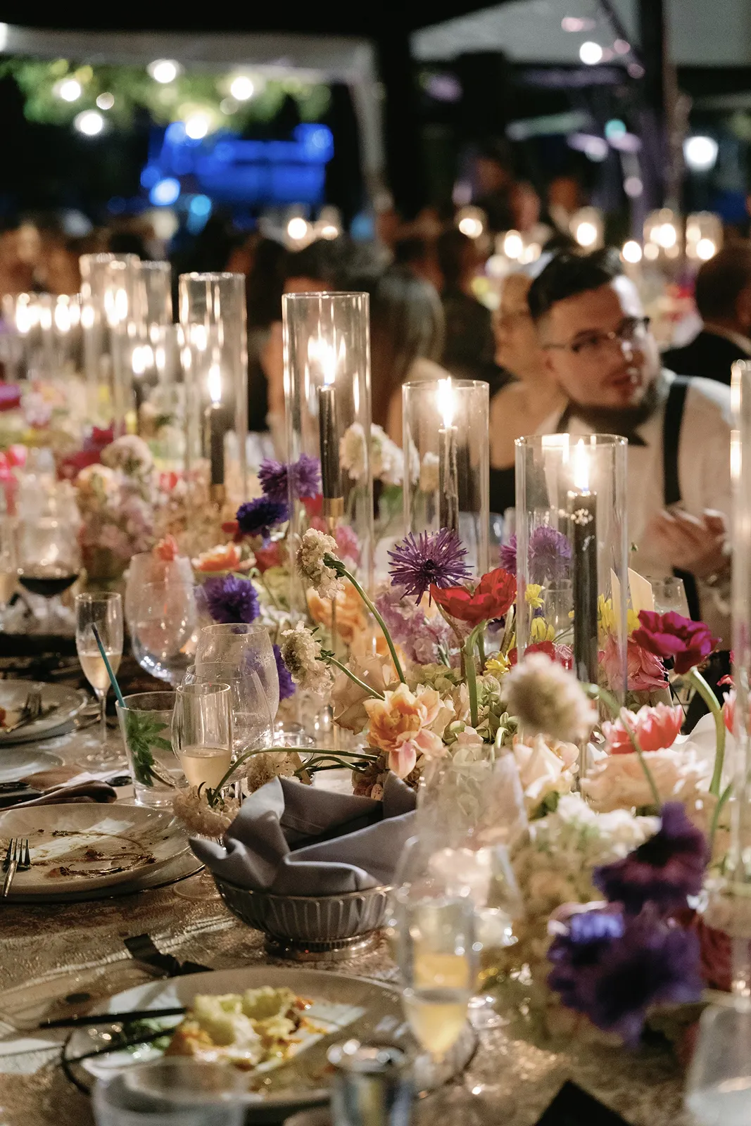 Long Fisher Island wedding reception table lined with glass candle holders, colorful florals, and guests enjoying dinner