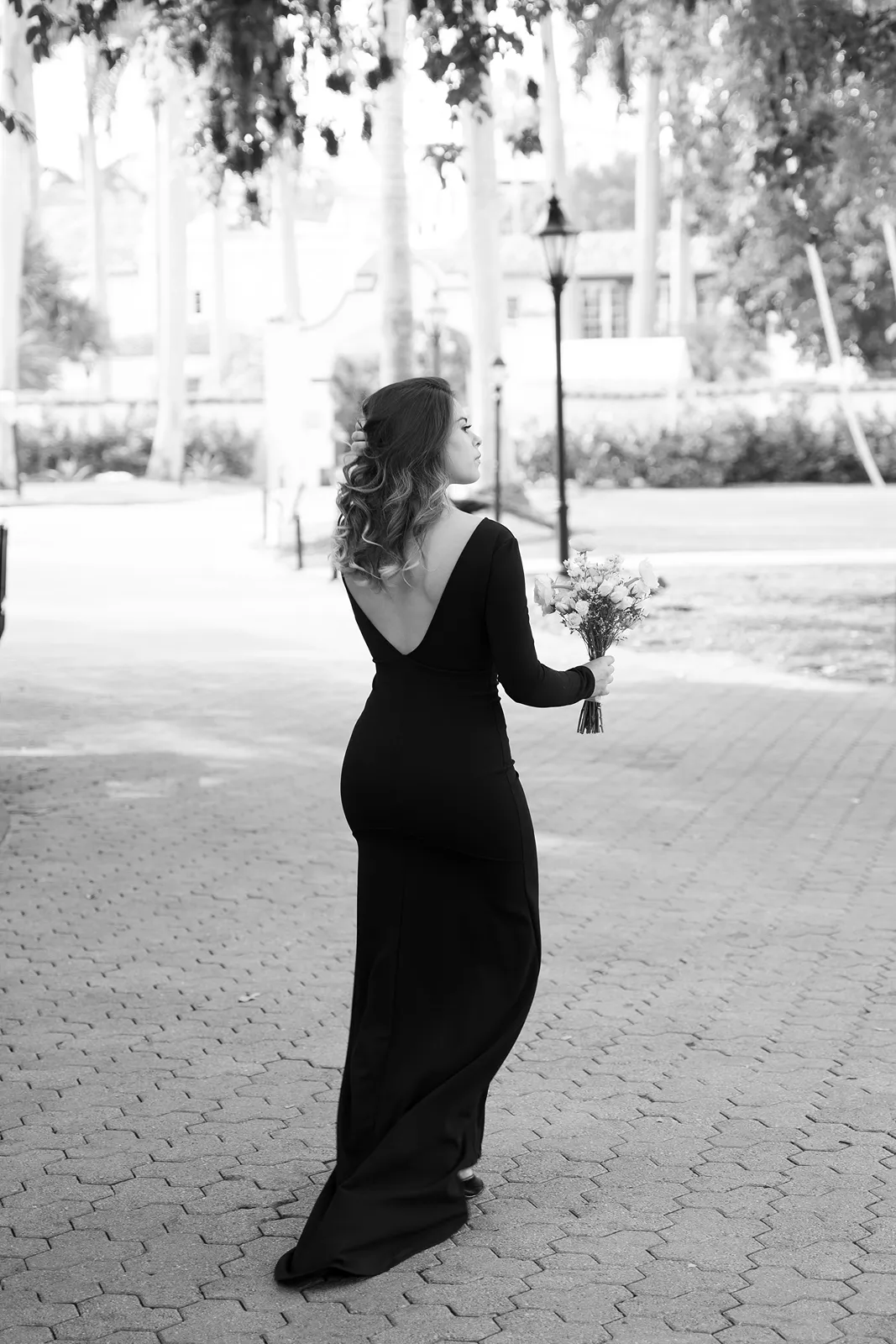 Black and white portrait of a bridesmaid in a long black dress holding a bouquet while walking outdoors
