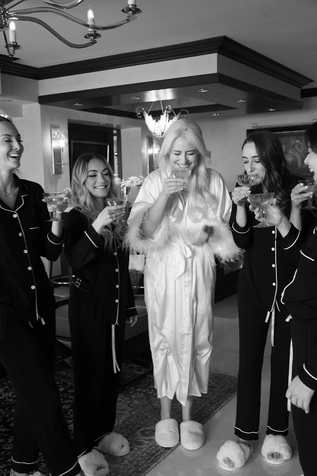 Black and white photo of bride and bridesmaids toasting drinks in matching pajamas