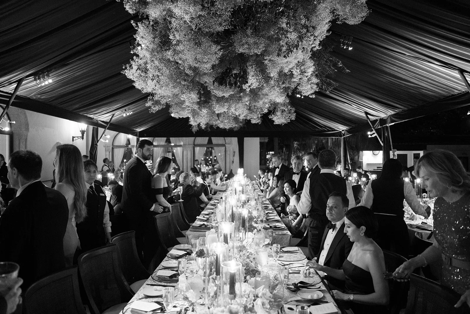 Black and white image of an elegant long table reception with candles and floral installation at a Fisher Island wedding