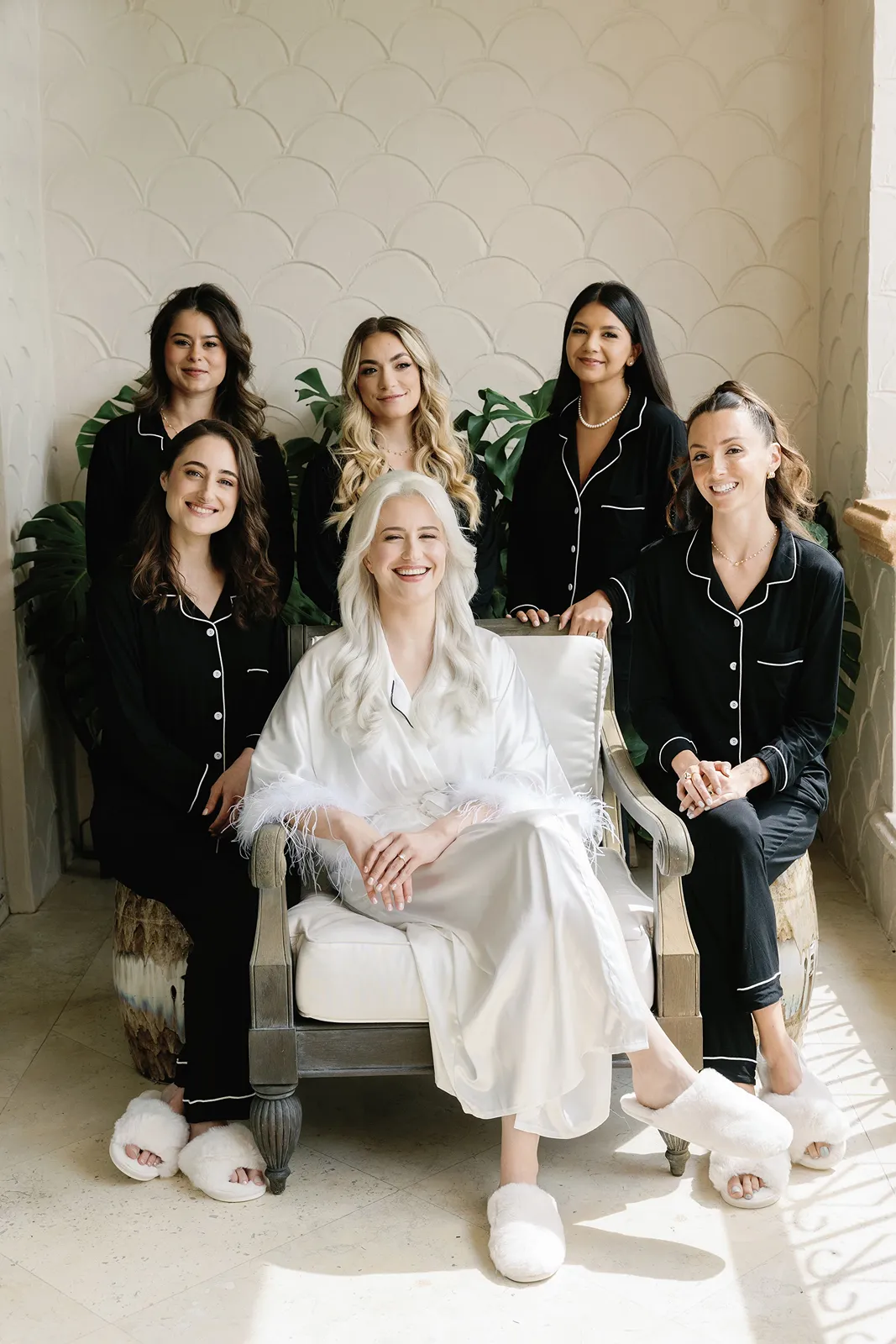 Bride seated and smiling with bridesmaids in matching black pajamas during getting ready moments