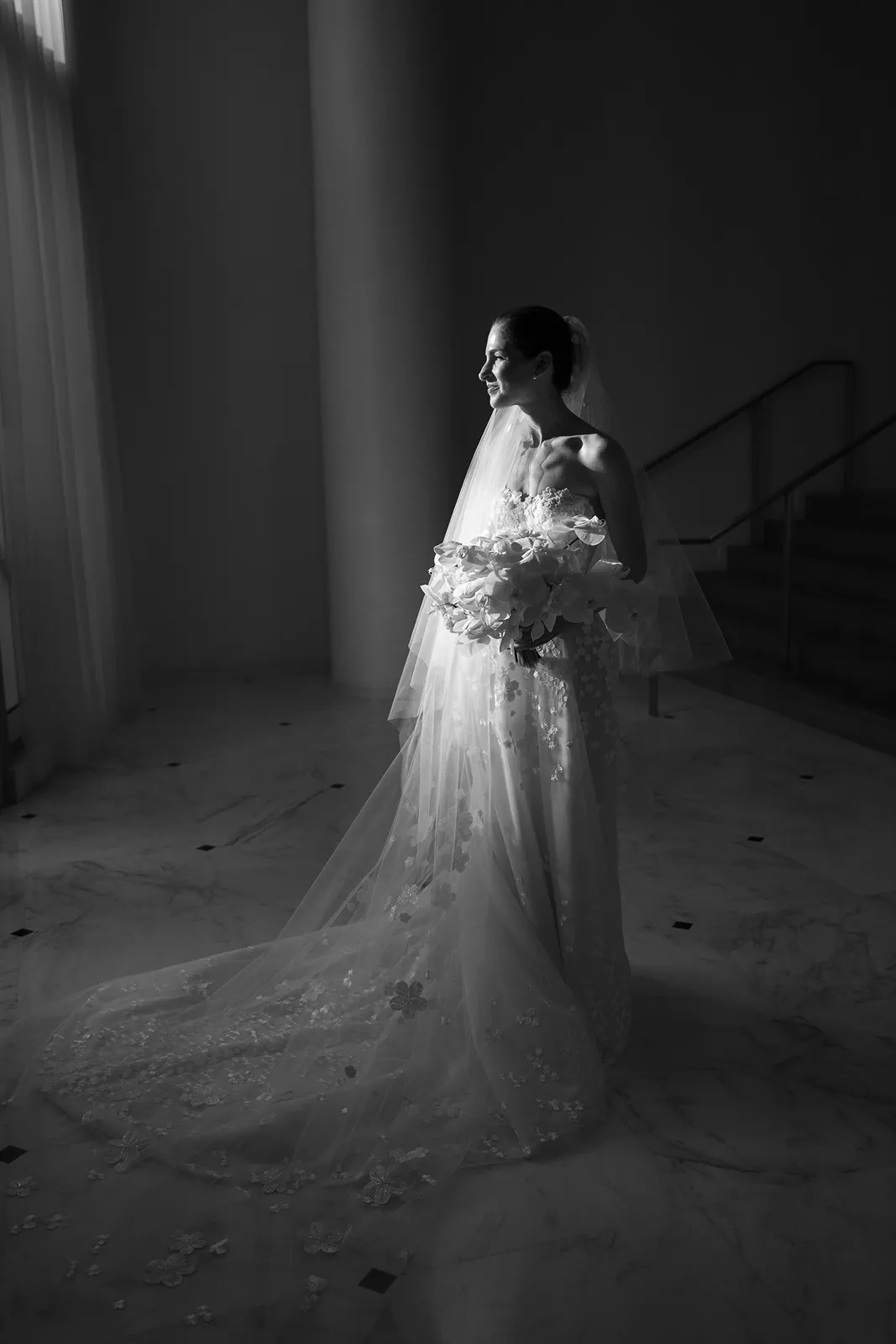 Bride in a strapless lace wedding gown holding a bouquet, photographed in dramatic window light at the Miami Beach EDITION