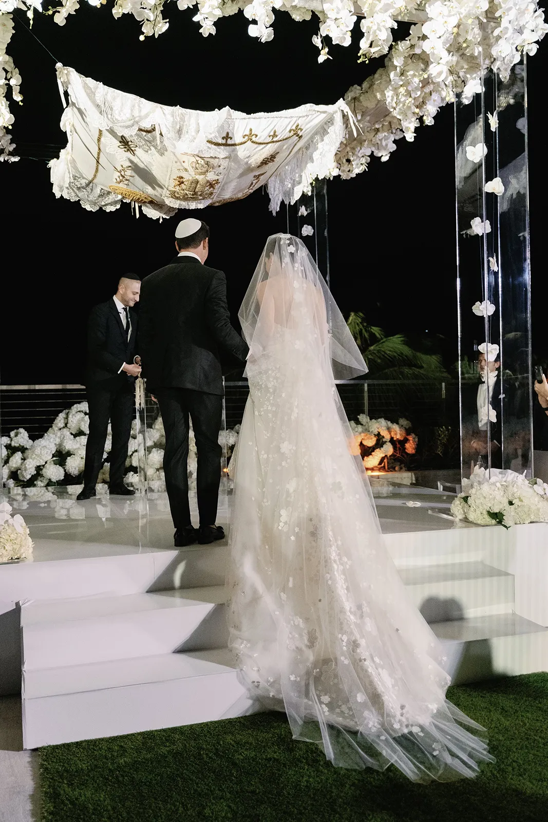 Bride and groom standing beneath a floral chuppah during an elegant evening wedding ceremony at the Miami Beach EDITION