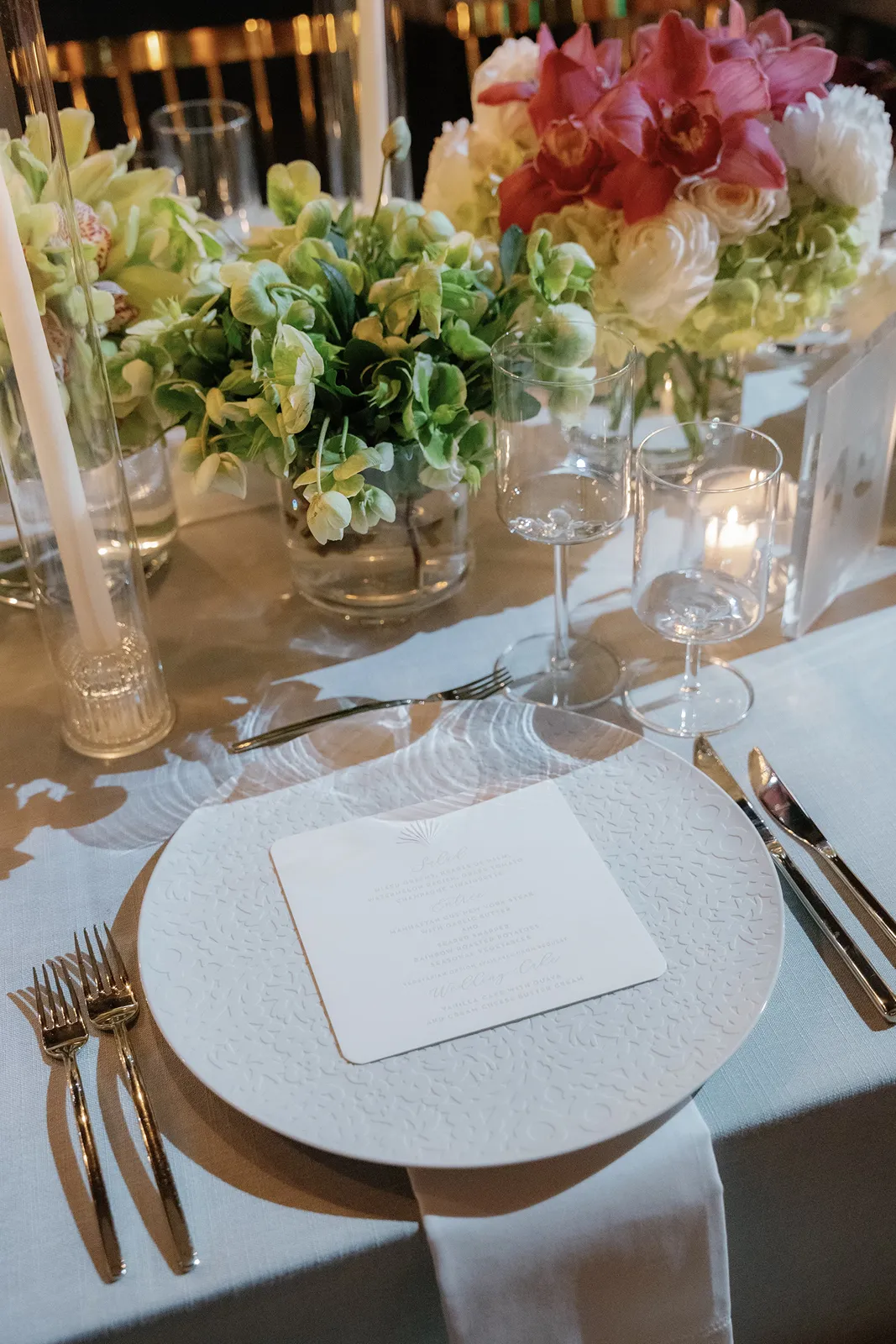 Elegant wedding reception table with white plates, candles, and lush floral centerpieces at the Miami Beach EDITION
