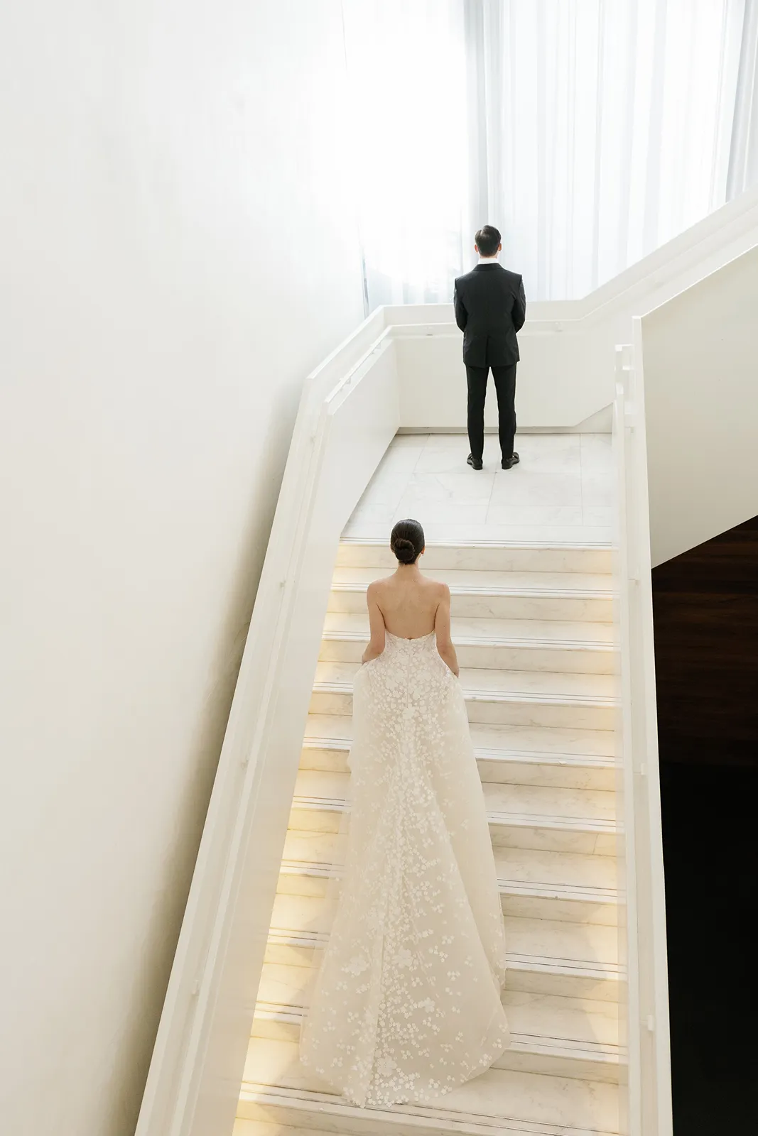 Bride walking up a modern white staircase toward the groom during a first look at the Miami Beach EDITION