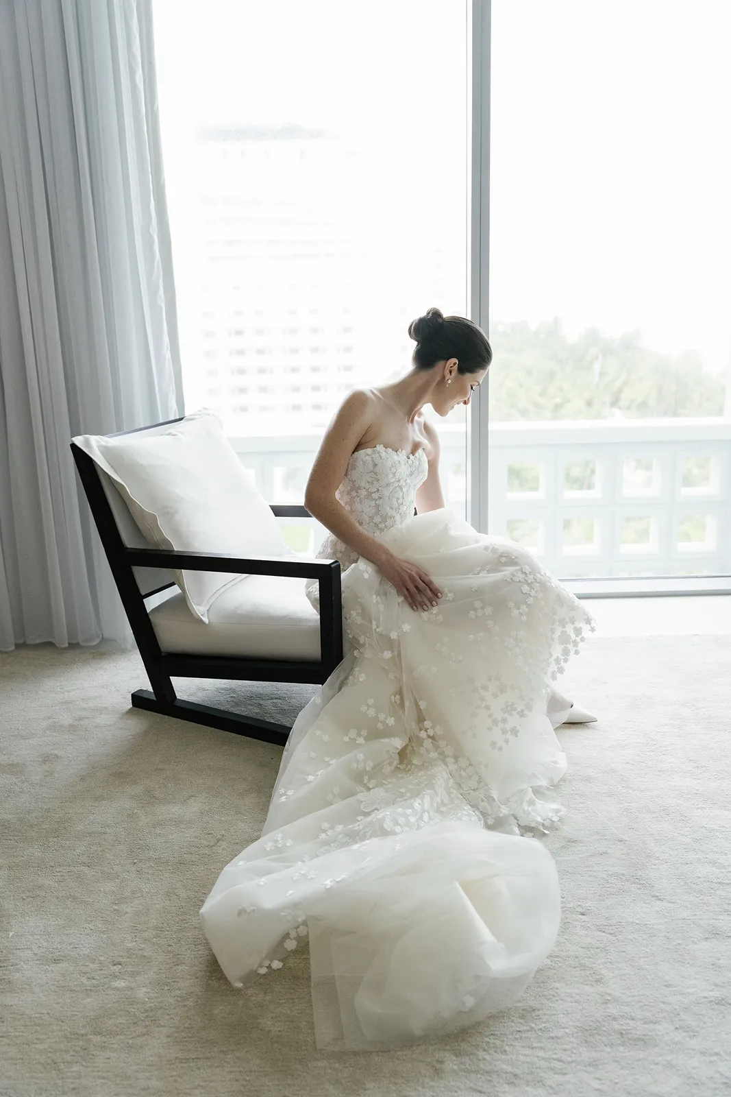 bride seated with soft window light behind as she puts her shoes on