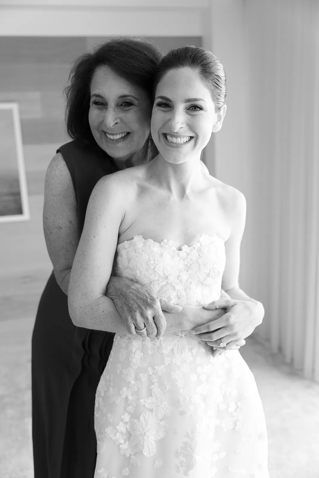 mother of the bride hugging the bride from behind after dress fitting