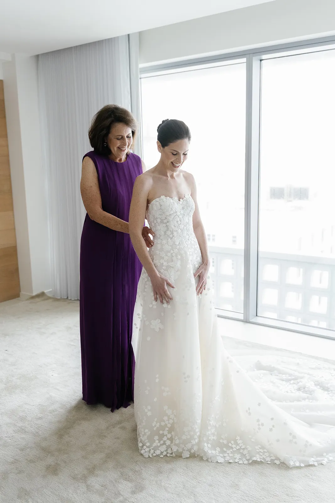 mother of the bride helping bride with dress while getting ready