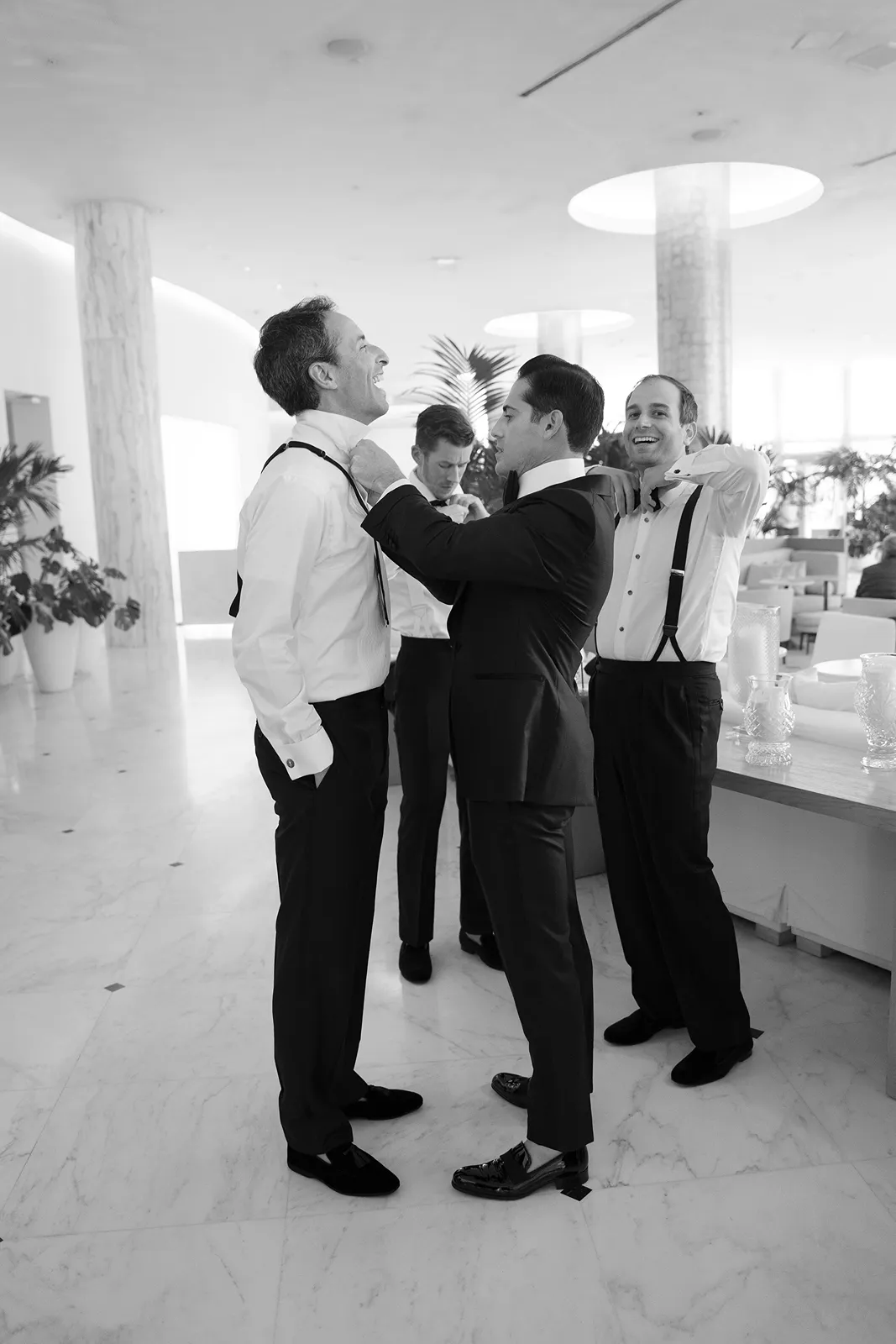 Groom helping a groomsman adjust his bow tie while the wedding party gets ready together
