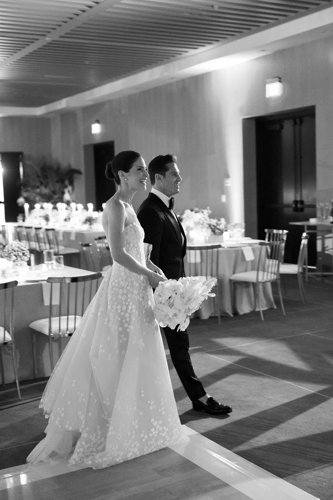 Bride and groom walking hand in hand into the reception space as guests look on