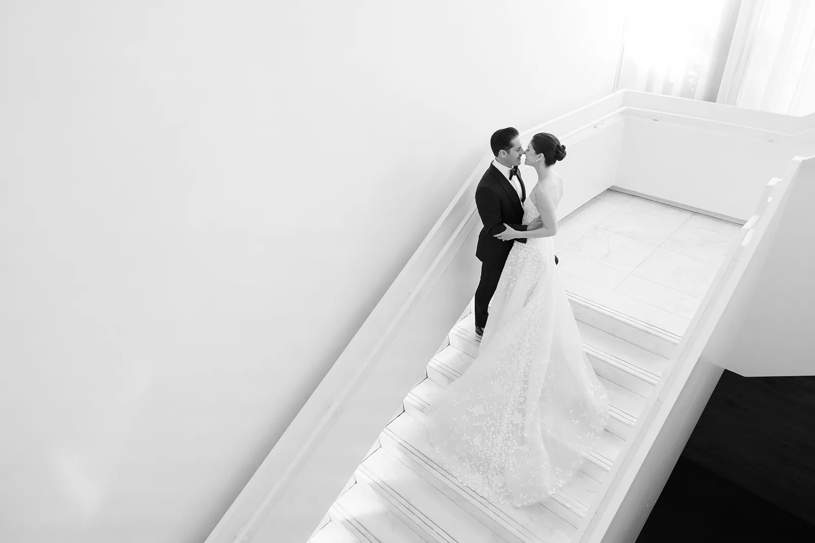 Bride and groom standing close together on a minimalist white staircase during a quiet portrait moment