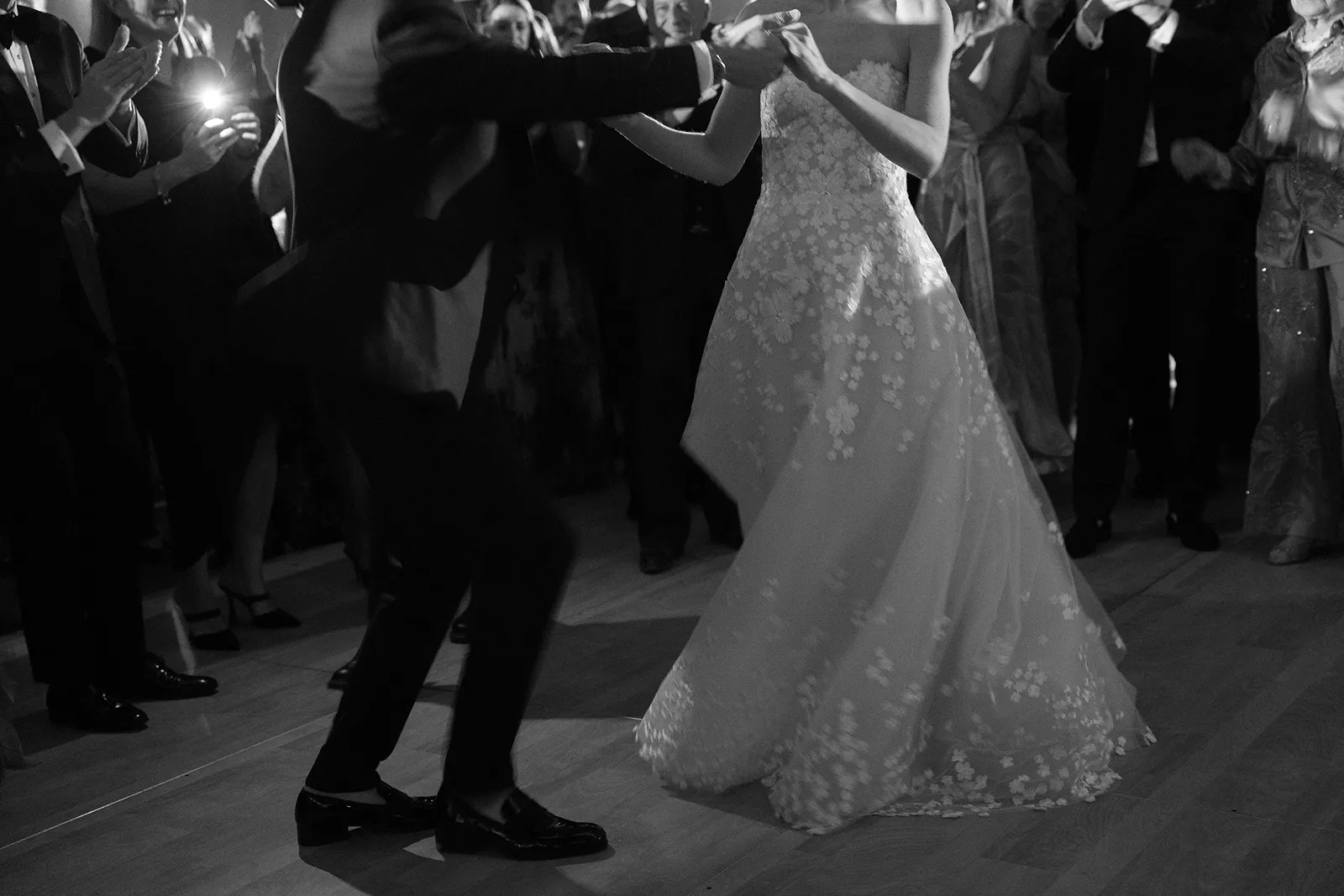 Close-up of the bride and groom dancing together as guests gather around the dance floor