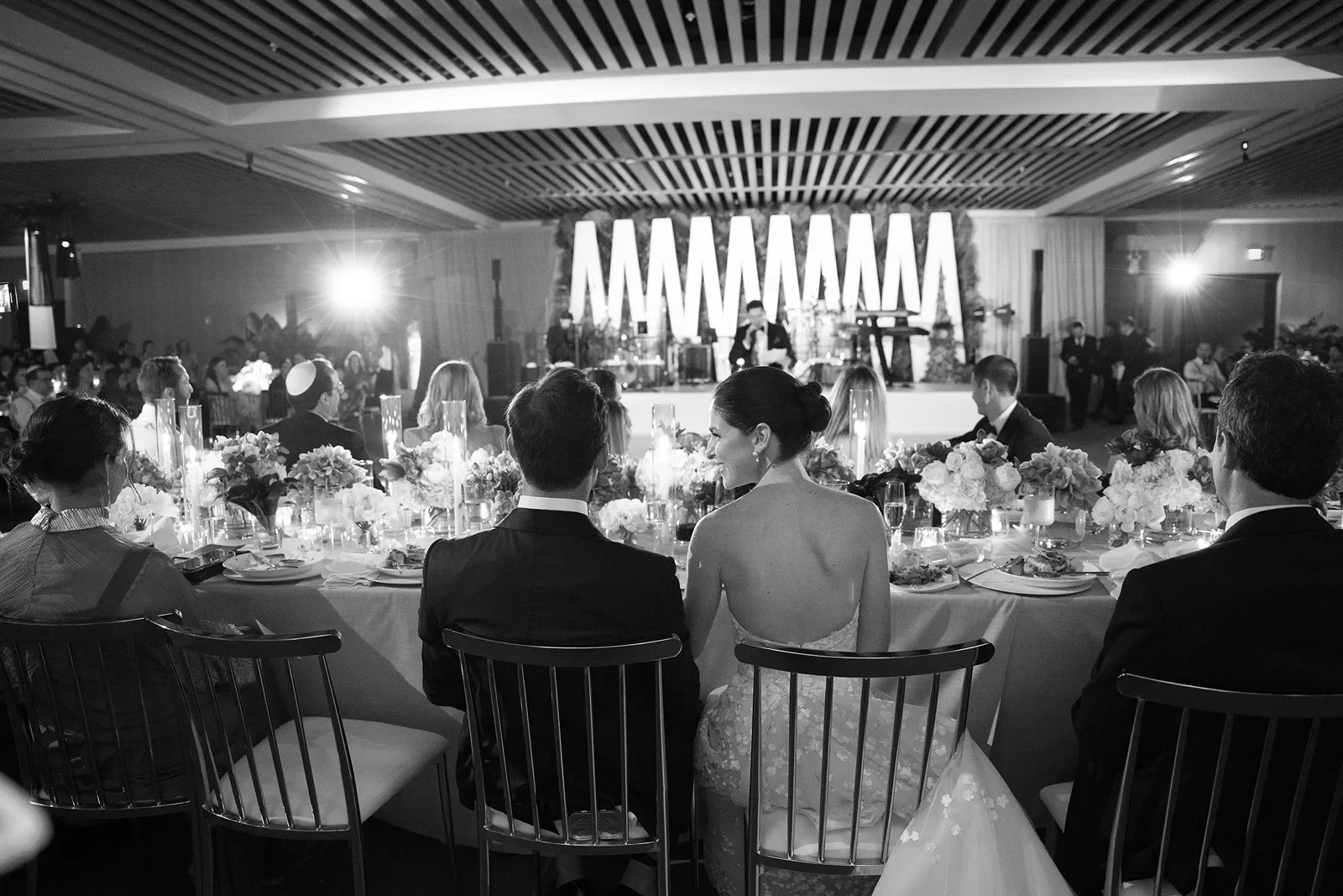 Bride and groom seated at the head table watching live music during the wedding reception