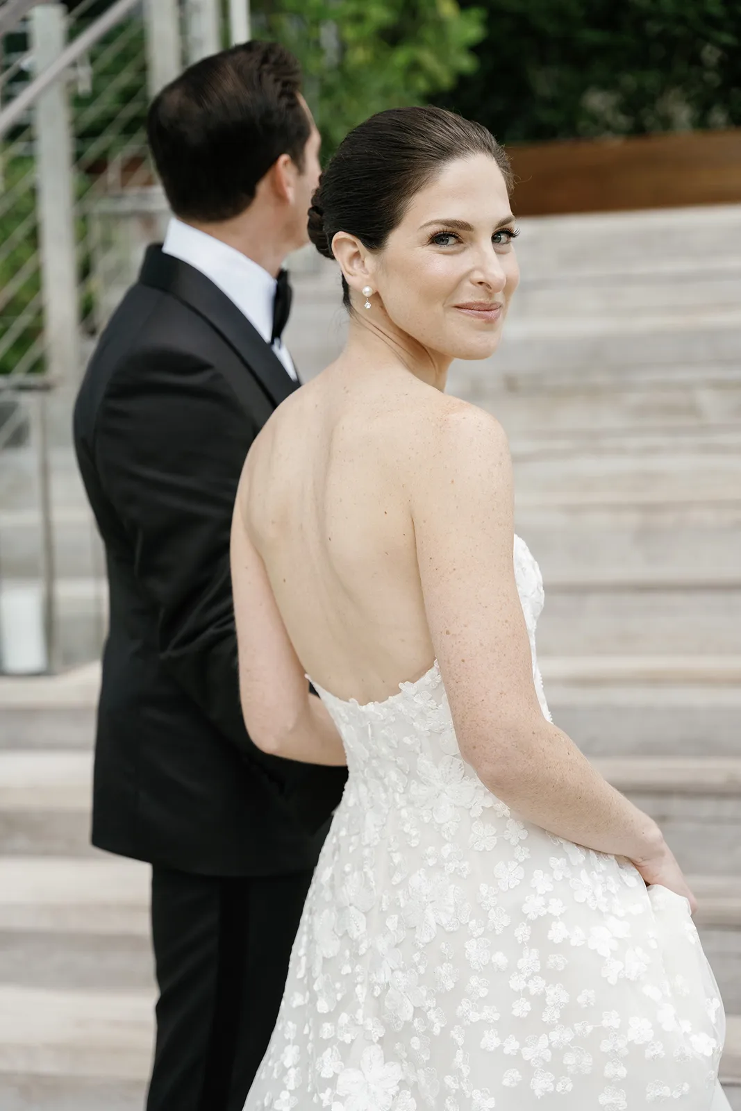 Bride glancing back with a smile while standing beside the groom in a strapless lace wedding gown