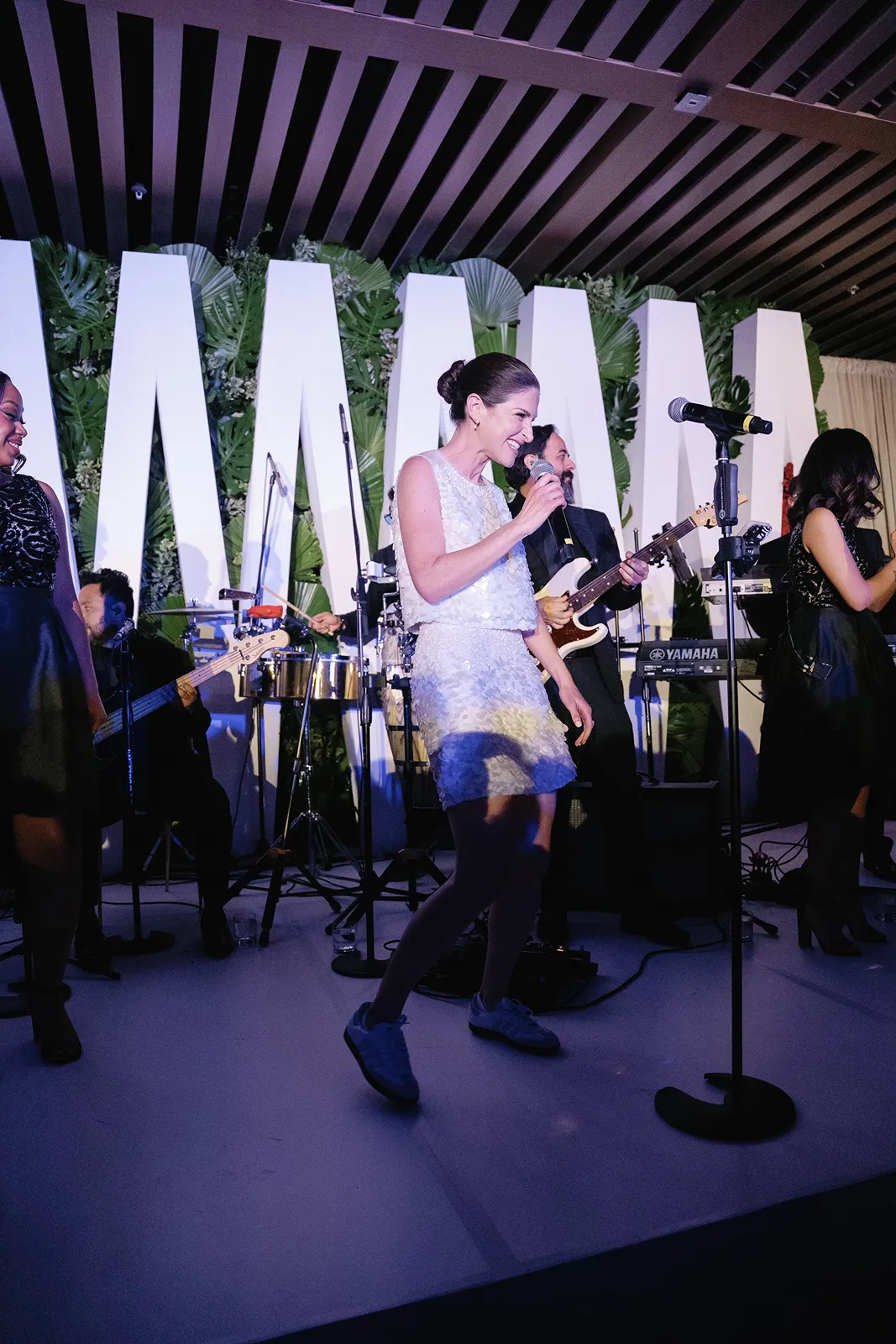 Bride singing into a microphone on stage with the live band during the wedding celebration