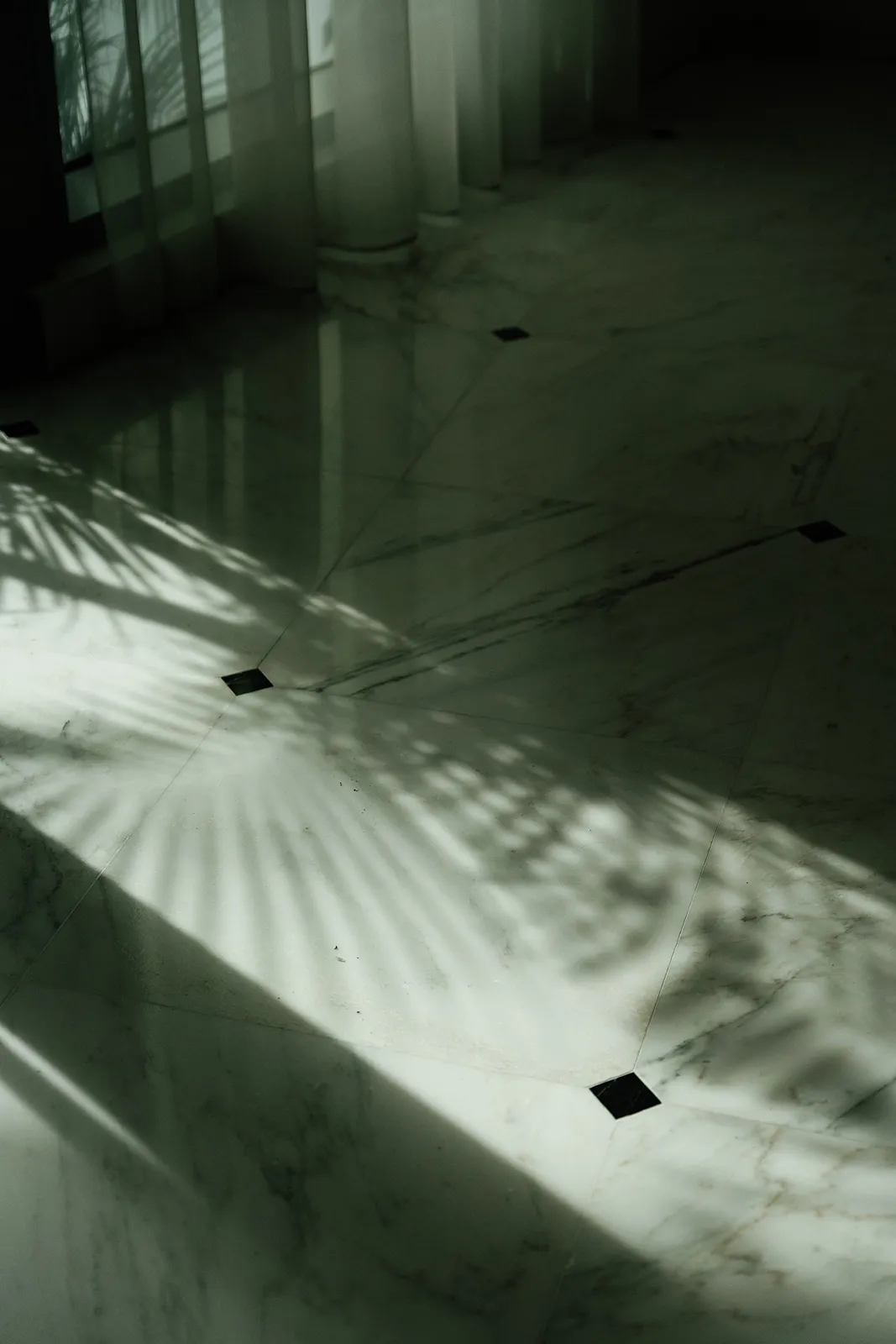 Soft natural light and shadows creating an abstract pattern across a marble floor