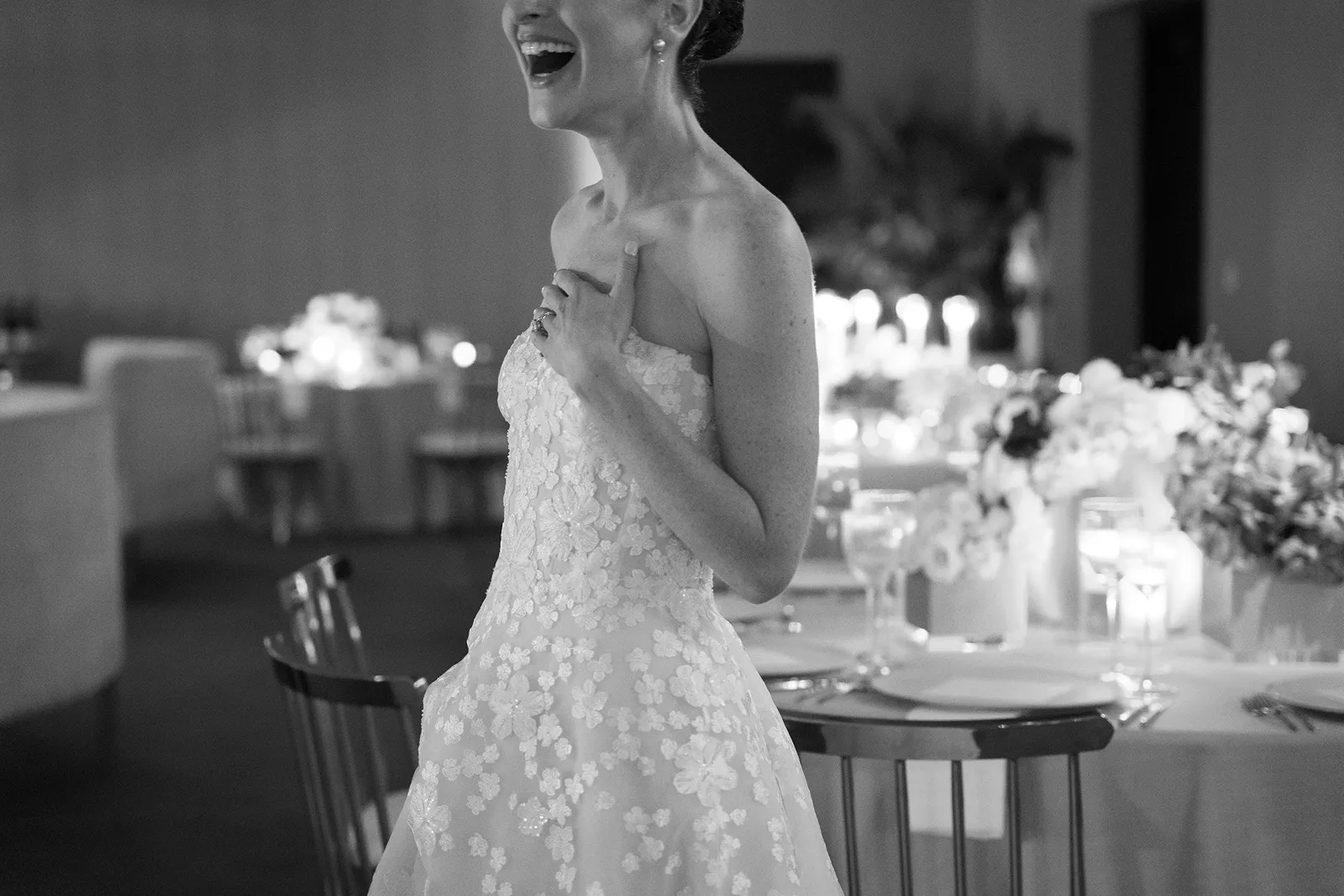 Bride laughing with her hand over her heart during an emotional moment at the wedding reception