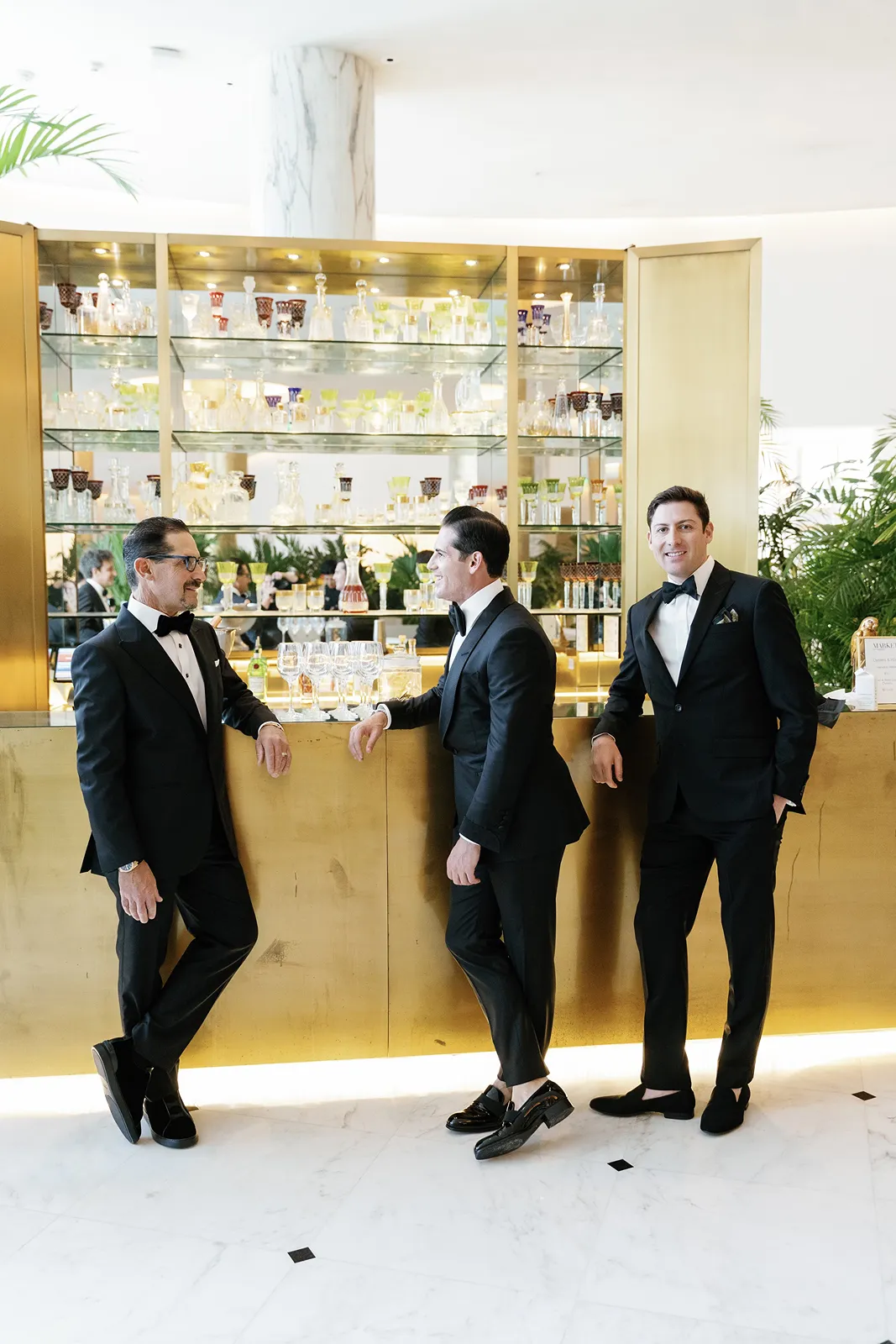 Three groomsmen in tuxedos standing together at a bar during pre-ceremony moments