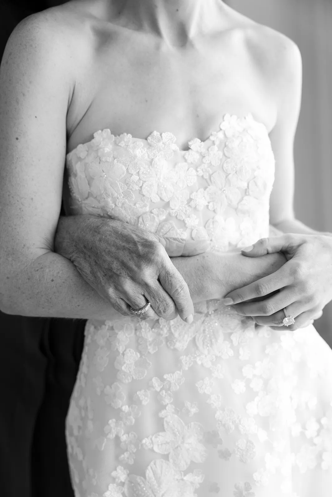 Close-up of the bride being embraced from behind, highlighting the lace texture of her wedding gown