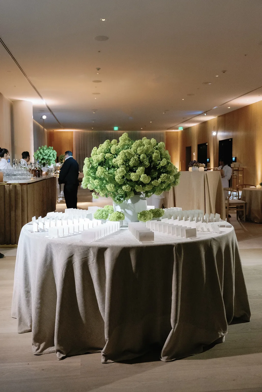 Wedding escort card display arranged around a large green floral centerpiece in a softly lit reception space