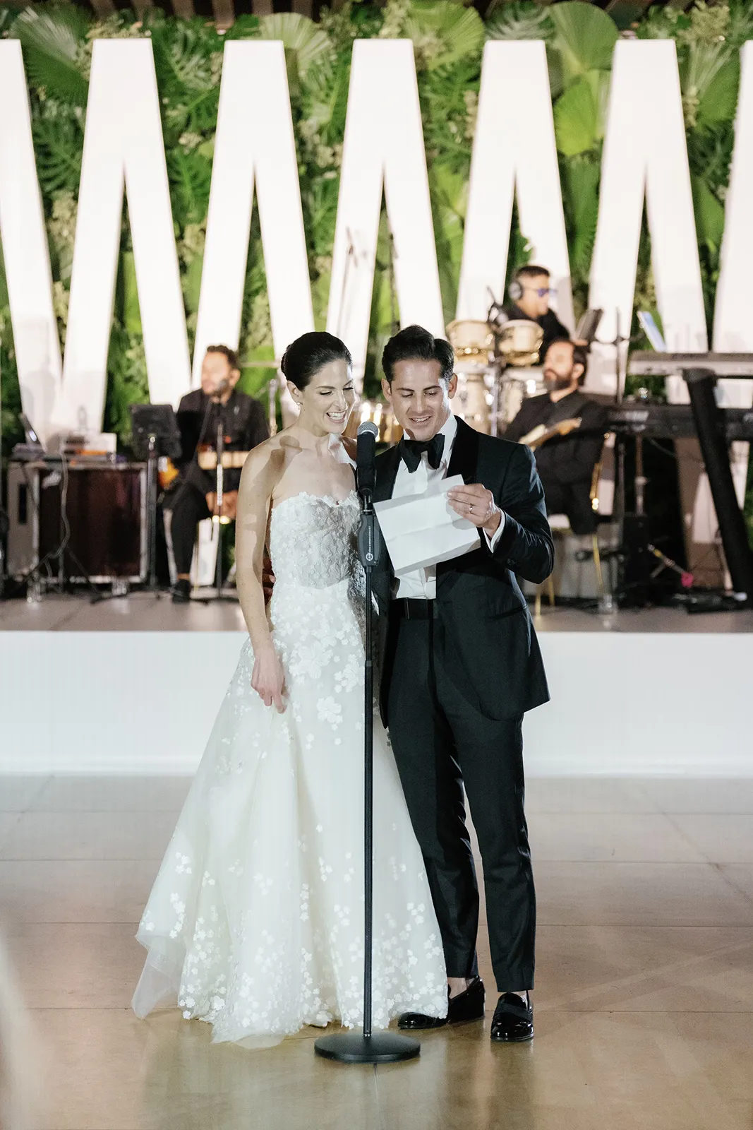 Bride and groom smiling as they read a speech together at the microphone during the wedding reception
