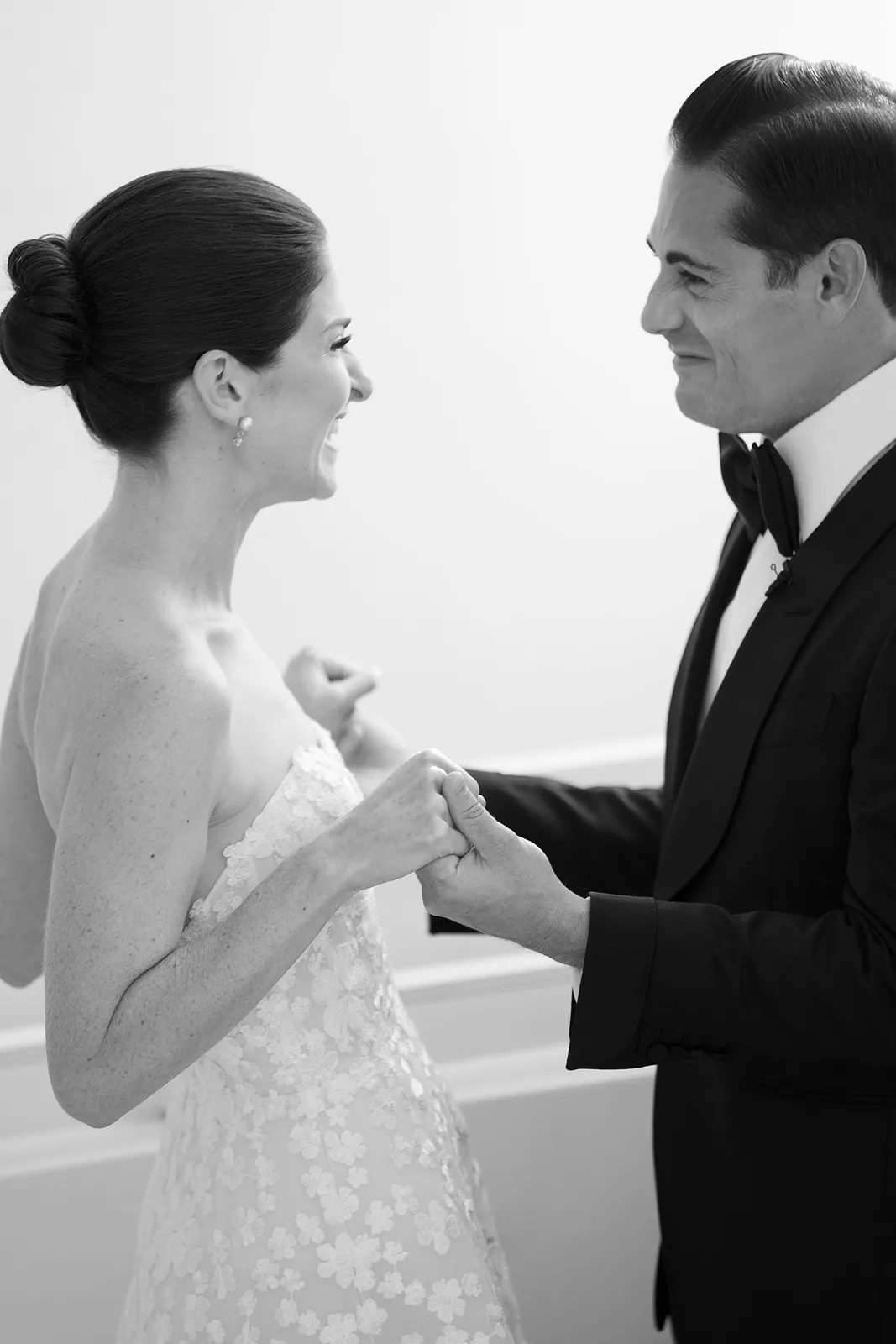 Bride and groom smiling at one another while holding hands during a quiet portrait moment