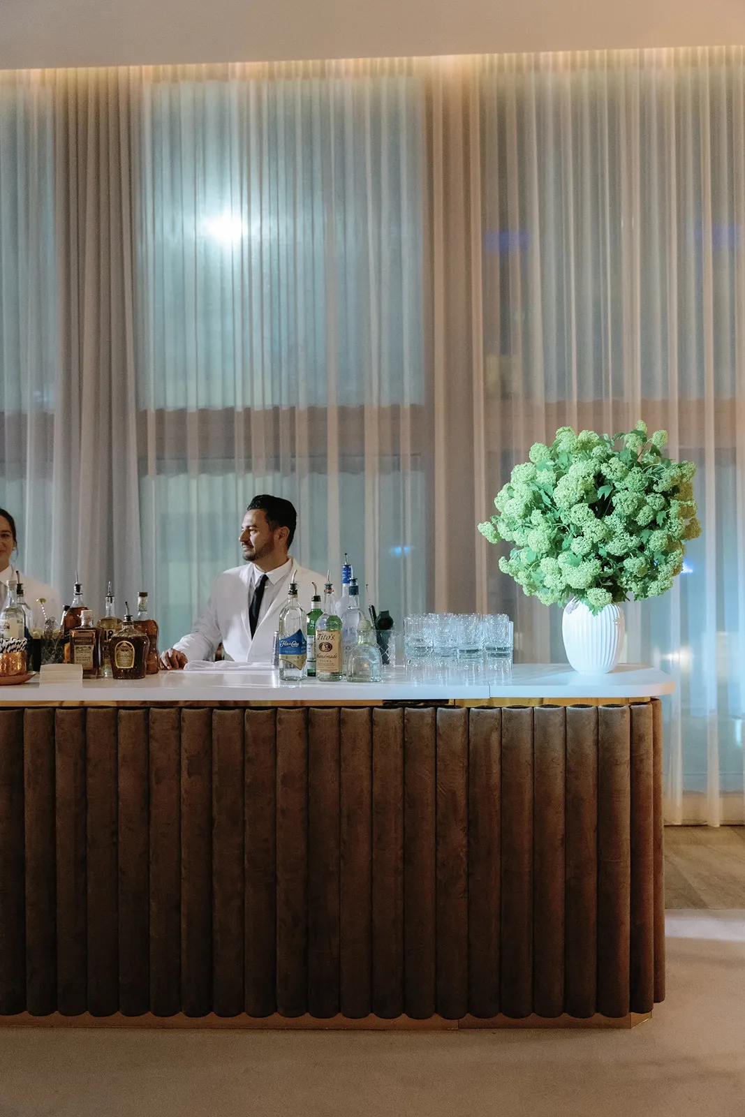 Elegant wedding cocktail bar with glassware, spirits, and a large green floral arrangement