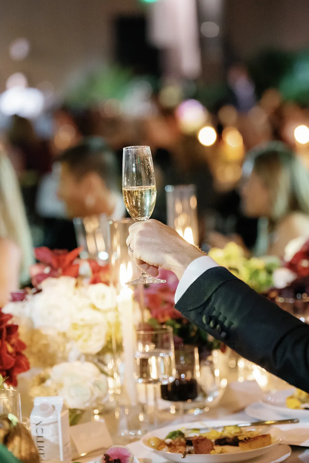 Guest raising a champagne glass during a candlelit wedding toast at the reception