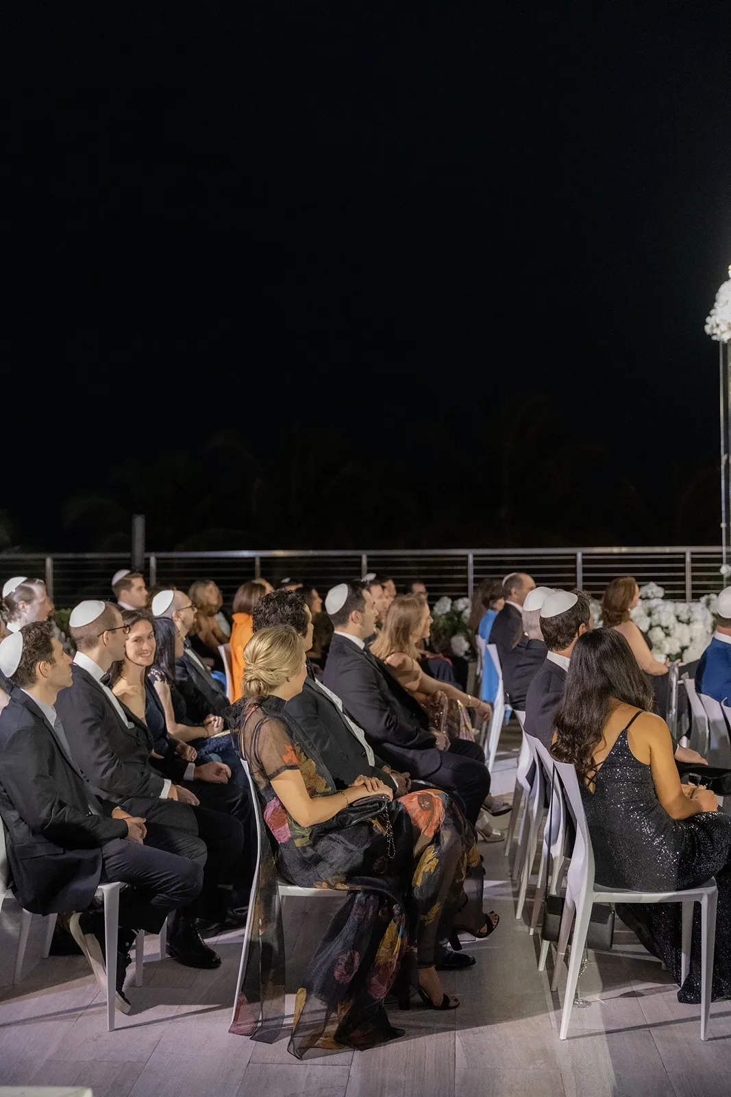 Wedding guests seated outdoors at night during the ceremony, facing the aisle