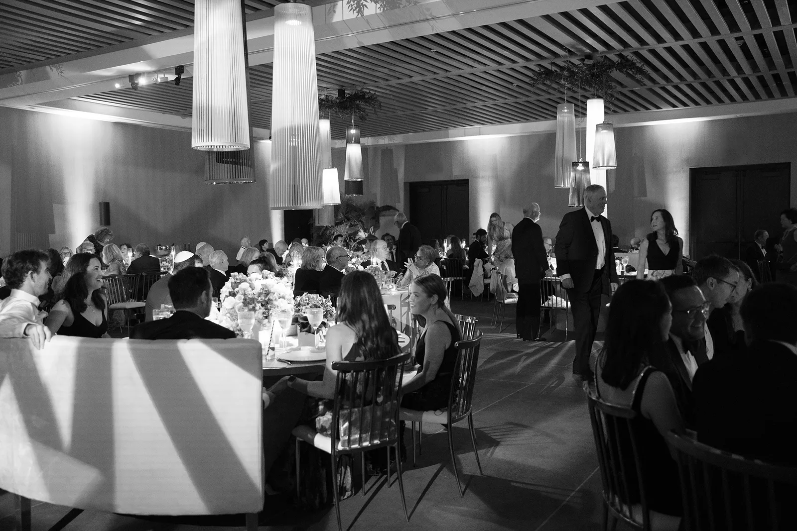 Wide view of the wedding reception with guests seated at candlelit tables beneath modern lighting