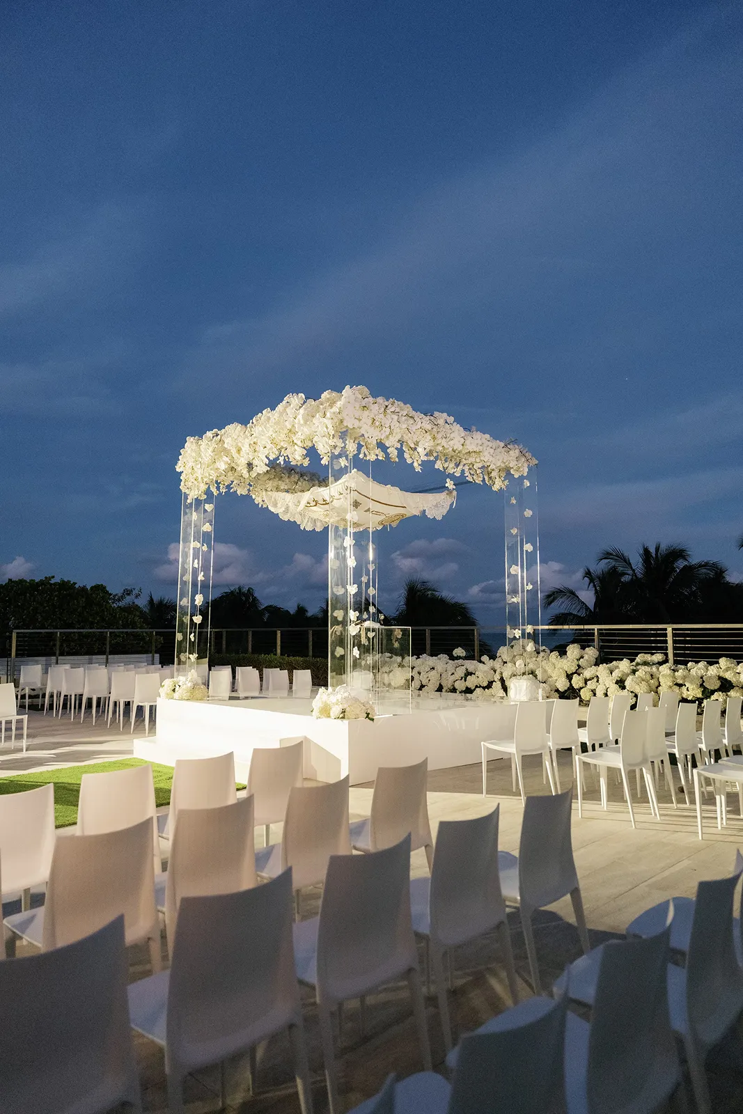 Outdoor wedding ceremony setup with a floral chuppah and white chairs at The Miami Beach EDITION at dusk
