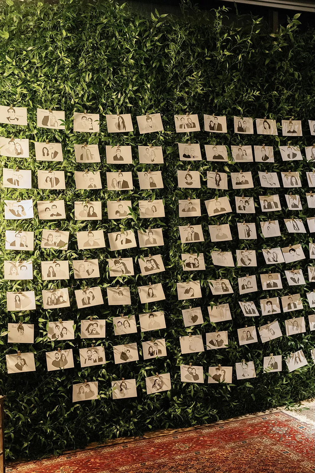 Escort card display featuring illustrated guest portraits arranged on a lush green wall