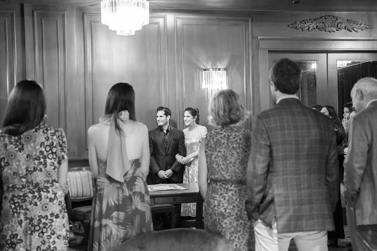 Bride and groom standing together as guests gather around during a rehearsal dinner moment