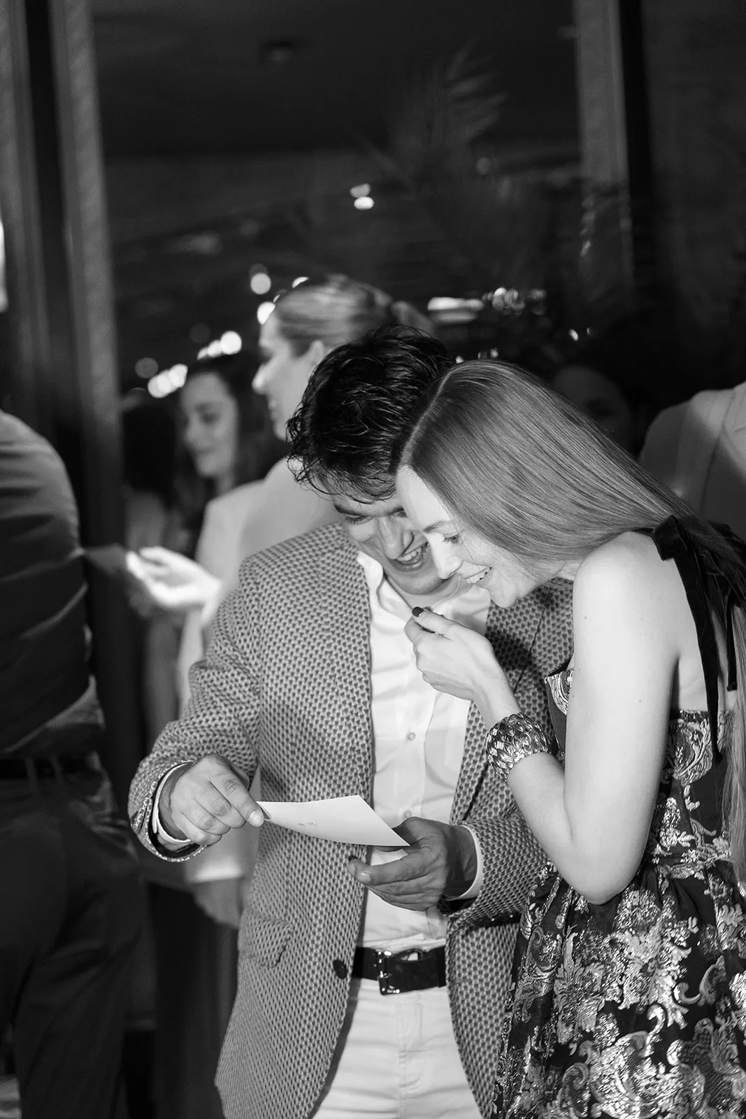 Guests laughing while reading a note during a rehearsal dinner at Hasalon Miami Beach