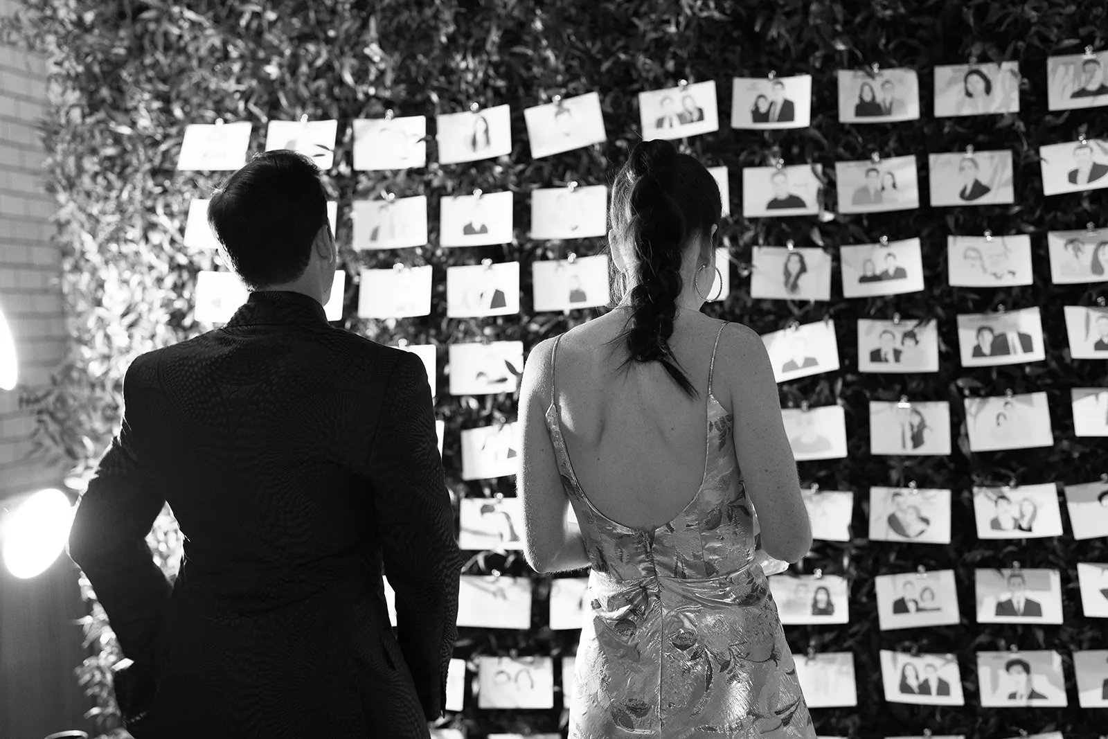 Bride and groom viewed from behind as they stand together in front of a wall of illustrated escort cards