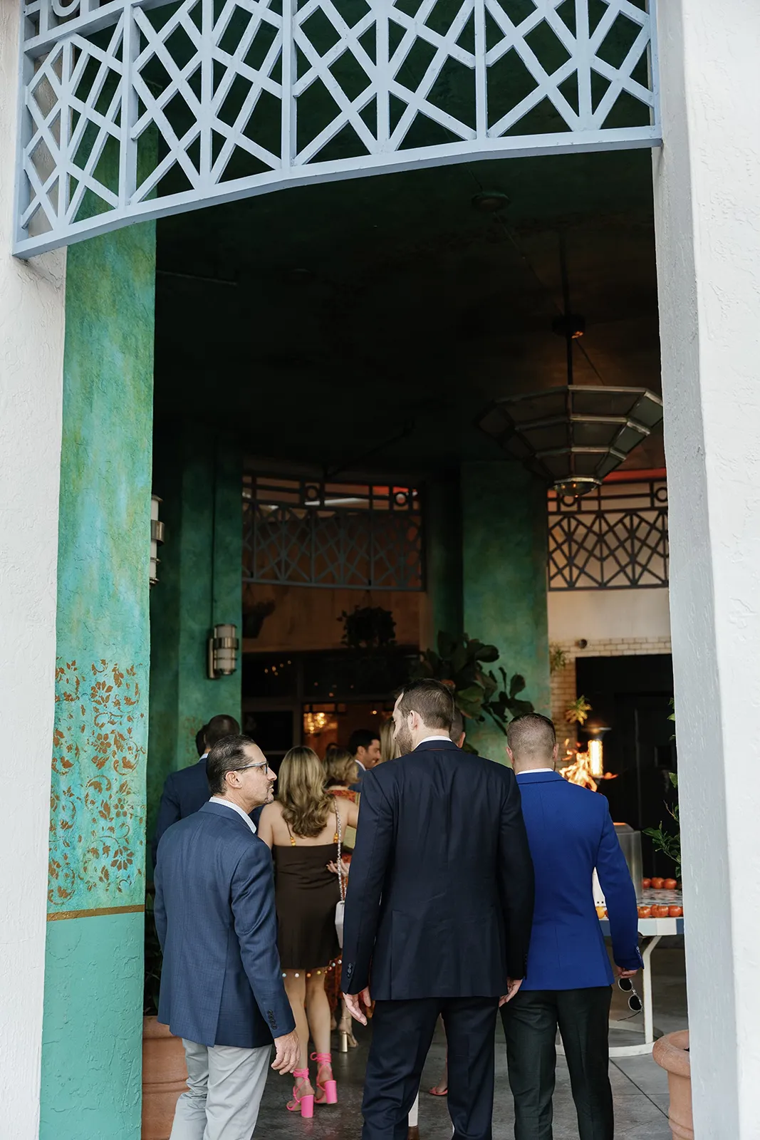 Guests arriving and mingling at a rehearsal dinner, walking through a colorful indoor courtyard space