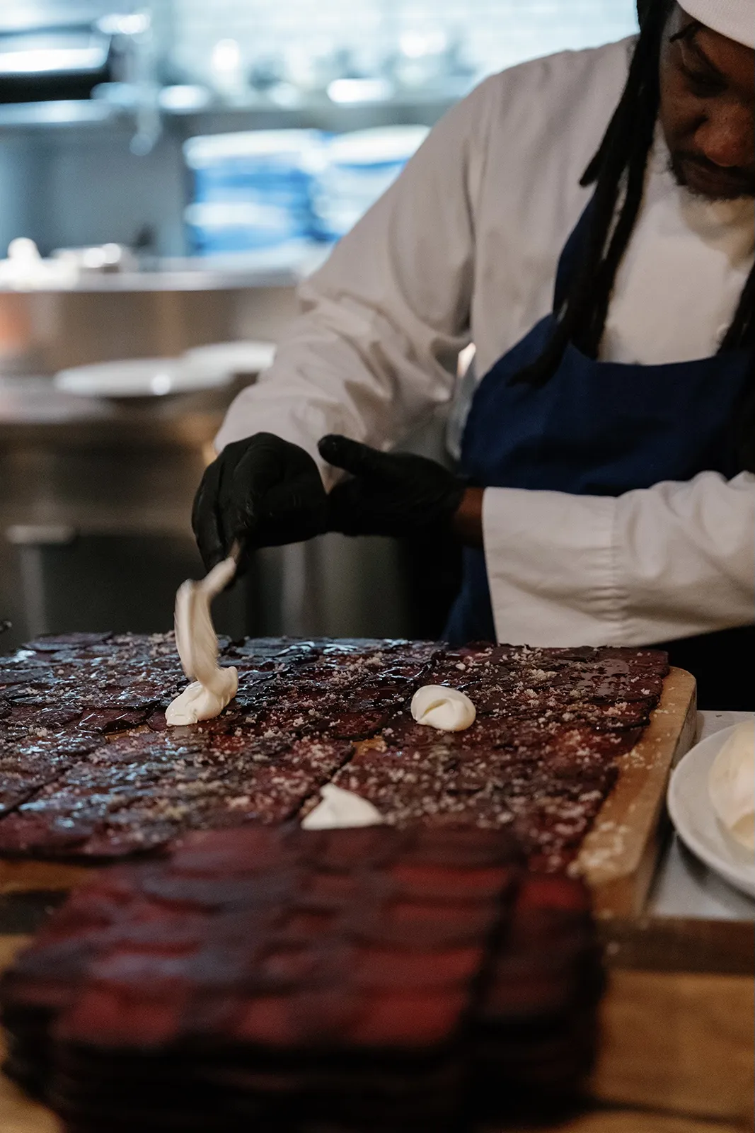 Chef plating sliced meat with finishing touches in an open kitchen during a wedding rehearsal dinner