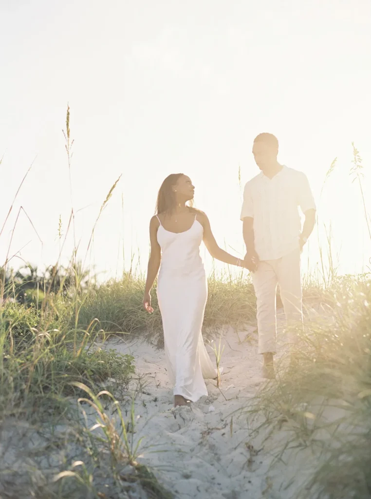 couple walking down a sand dune with a sunset glow behind them