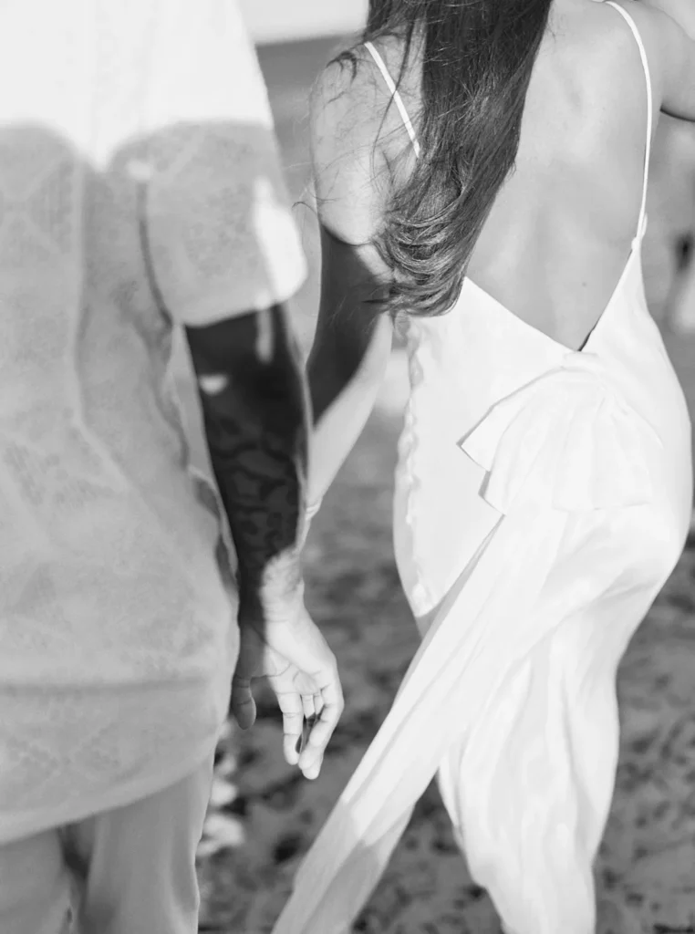 the back of a couple walking away as the breeze lifts the bride's dress details