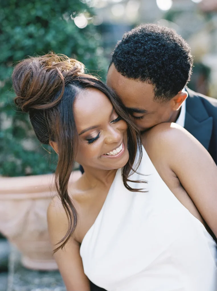 groom giving his fiancé a hug from the back and kissing her cheek