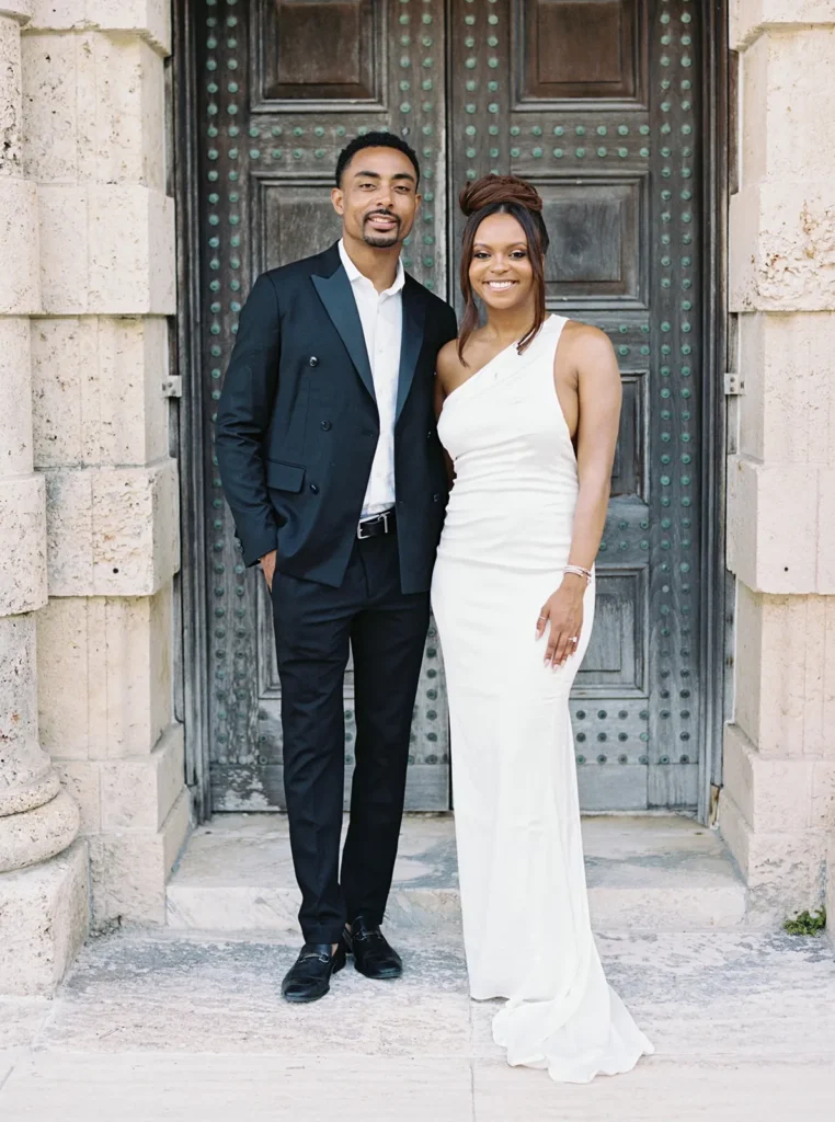 couple smiling in front of a dark iron door in vizcaya museum