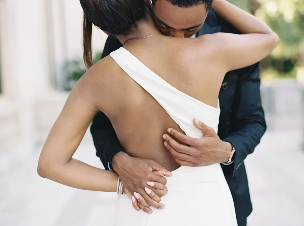 groom giving his fiancé a hug as he also kisses her neck