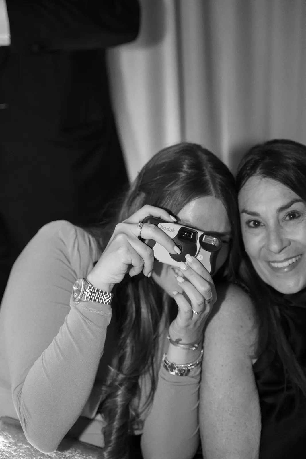 Guests laugh and pose while taking photos with a disposable camera during a lively wedding after-party