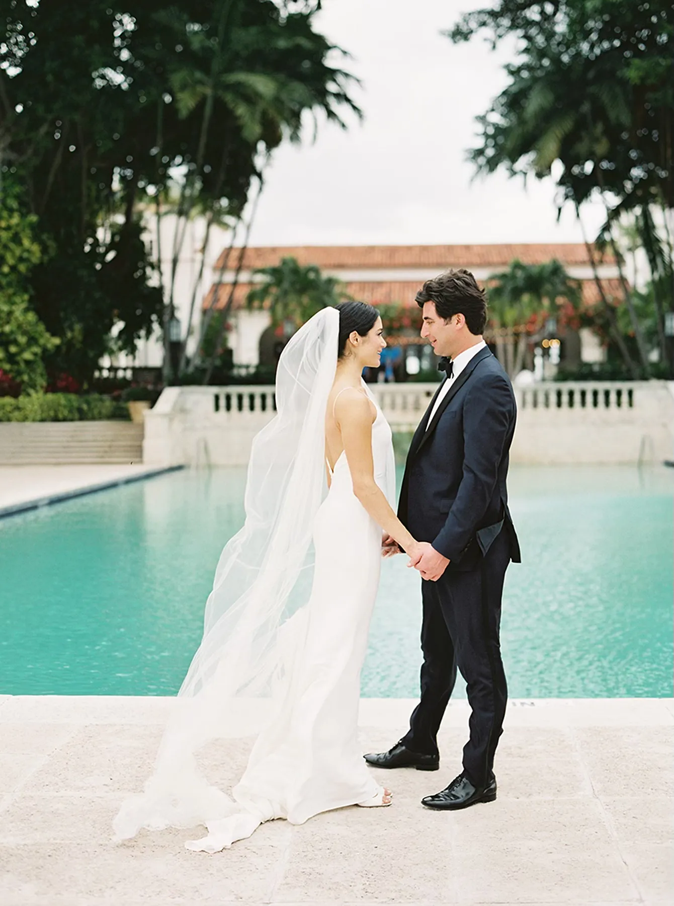 bride and groom holding hands during portraits with pool behind them in Indian creek country club