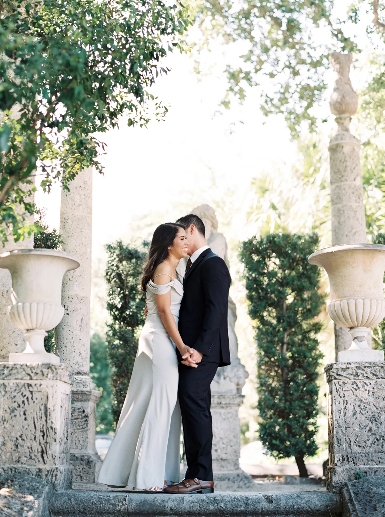 Couple sharing an intimate moment beneath stone columns surrounded by greenery